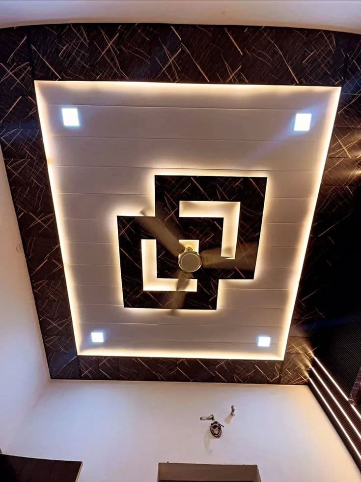 PVC false ceiling in dark stone-pattern finish with layered LED lighting design and ceiling fan